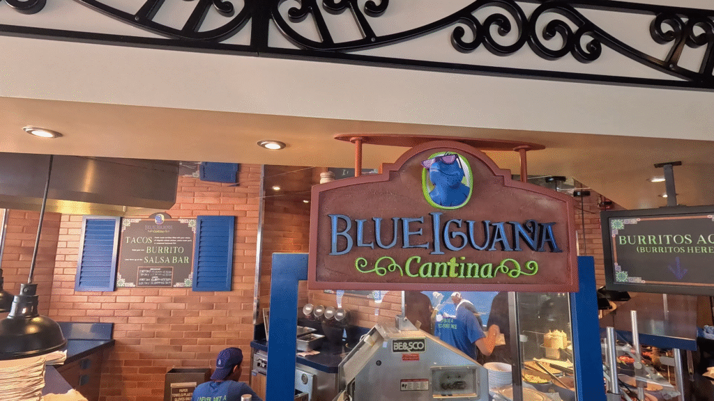 The vibrant sign and serving area of the Blue Iguana Cantina on the Carnival Dream, showcasing the complementary tacos and burritos menu options.