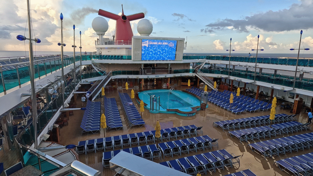 Lido Pool Area: Aerial view of the Carnival Dream's Lido Deck, showing the main pool, large movie screen, and rows of blue sun loungers under the red funnel.