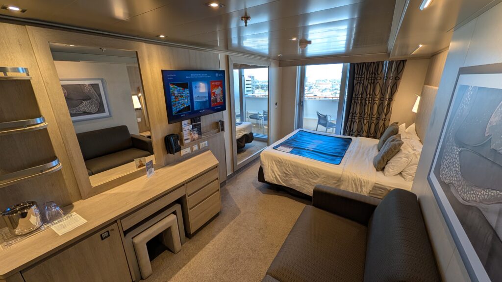 MSC Seascape balcony cabin 10024 interior showing king bed, sofa, vanity desk, TV, and balcony doors on Deck 10