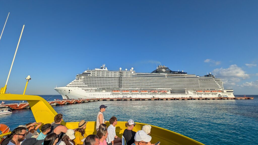 Passengers aboard the ferry departing Cozumel, Mexico, with MSC Seascape docked at the cruise pier as the ferry heads toward Playa del Carmen on a sunny Caribbean day.