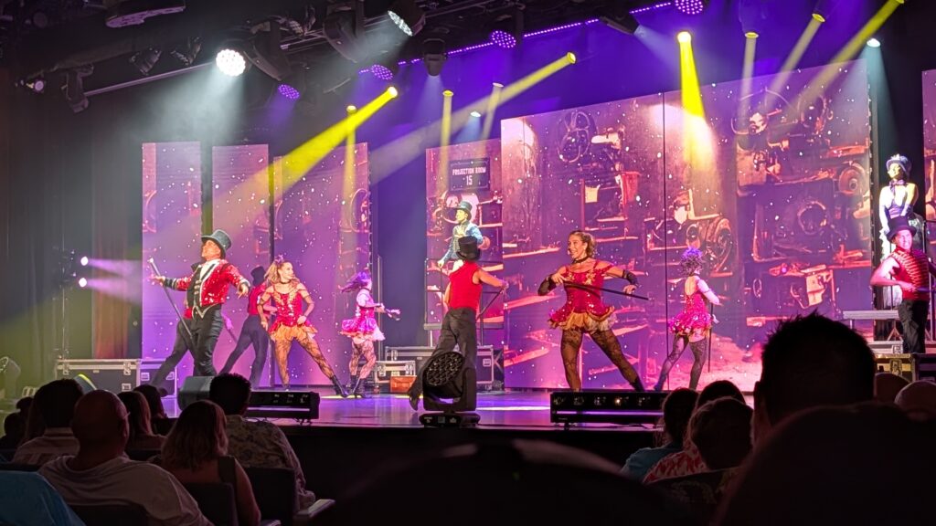 Performers on stage during a production show in the Chora Theatre aboard MSC Seascape, featuring colorful costumes, dancers, singers, and large digital screens.