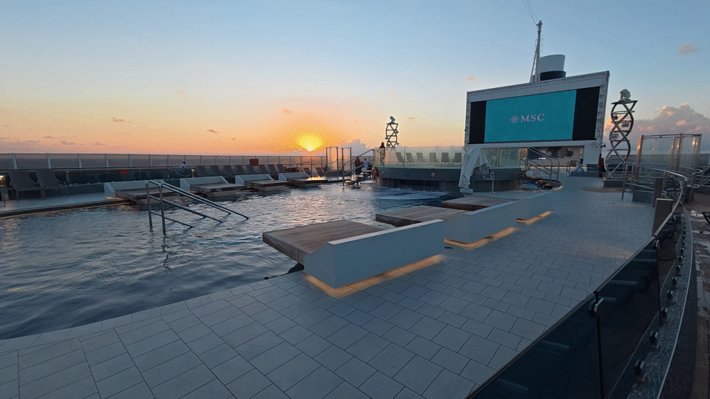 Morning sunrise view over the MSC Seascape Marina Pool area, showing the large LED screen and Google wall backdrop as the ship’s outdoor deck comes to life at sea.