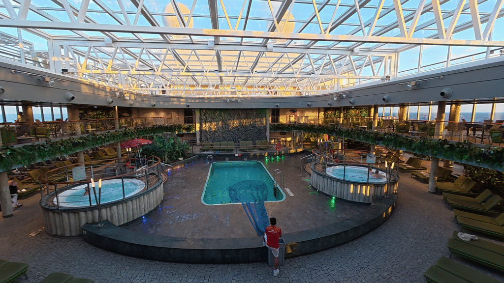 MSC Seascape Jungle Pool area with retractable roof open, featuring two hot tubs, surrounding lounge seating, and a lush indoor tropical-style design.