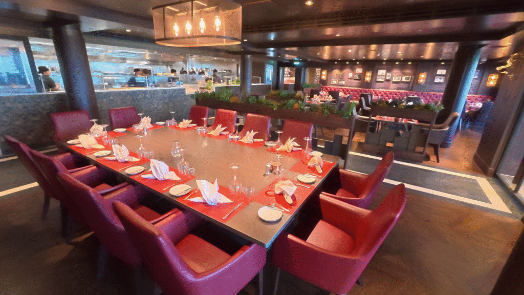 MSC Seascape Butcher’s Cut Steakhouse interior with red leather seating, visible open kitchen, and a mix of small and large tables in a sophisticated dining setting.