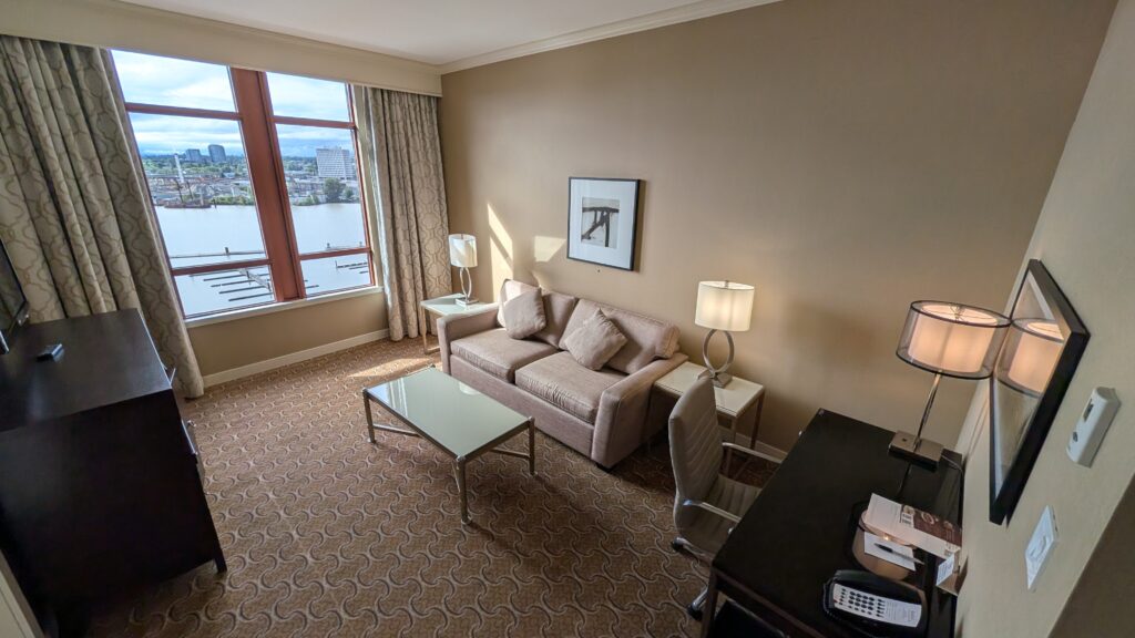 Spacious living room inside the 1 Bedroom Marina View Suite at the River Rock Casino Resort, featuring a couch, coffee table, workstation, TV, and Fraser River views.