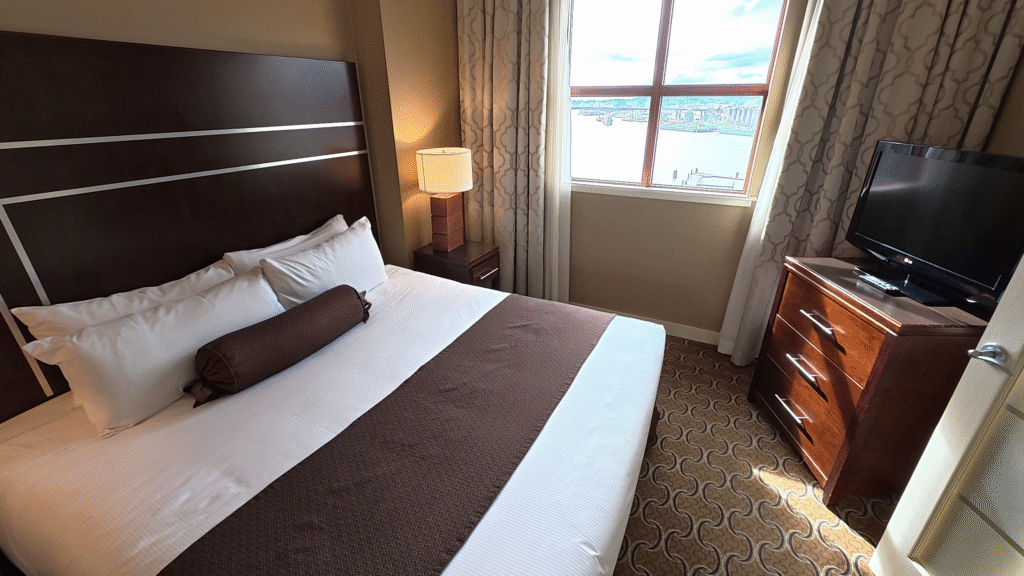 King bedroom in the 1 Bedroom Marina View Suite at the River Rock Casino Resort, featuring a comfortable bed, TV, closet, and views of the Fraser River.