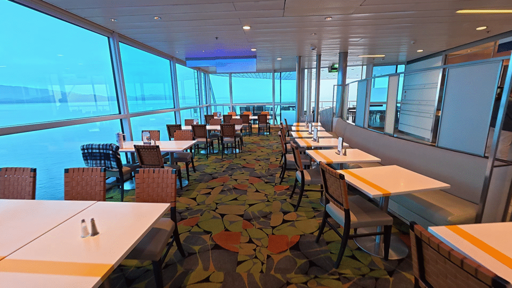 Seating area inside the Oceanview Café aboard Celebrity Solstice with large panoramic windows overlooking Alaska.