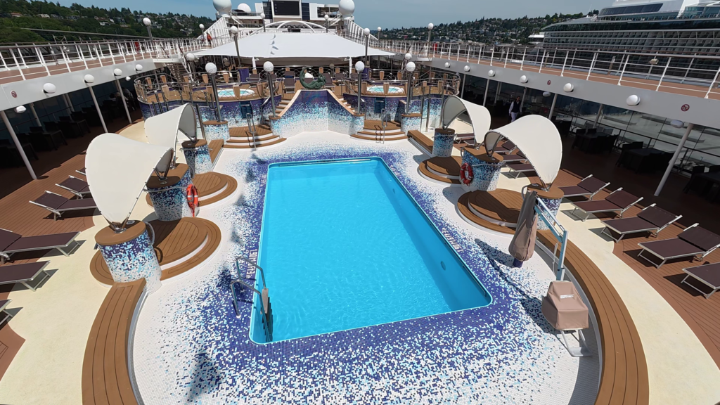 MSC Poesia outdoor pool deck with swimming pool, elevated whirlpools, loungers, and stage area.