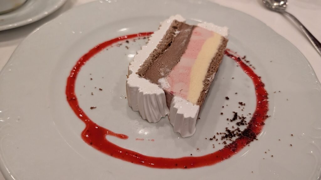 Slice of Baked Alaska dessert with colourful layers and red sauce aboard MSC Poesia.