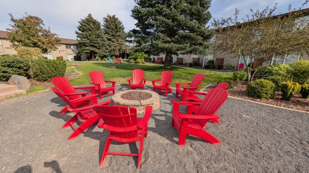 Outdoor courtyard with red Adirondack chairs surrounding a stone fire pit at Ramada by Wyndham Spokane Airport.