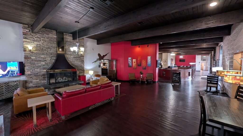 Restaurant and dining area at Ramada by Wyndham Spokane Airport featuring a stone fireplace, exposed wooden beams, and comfortable seating.