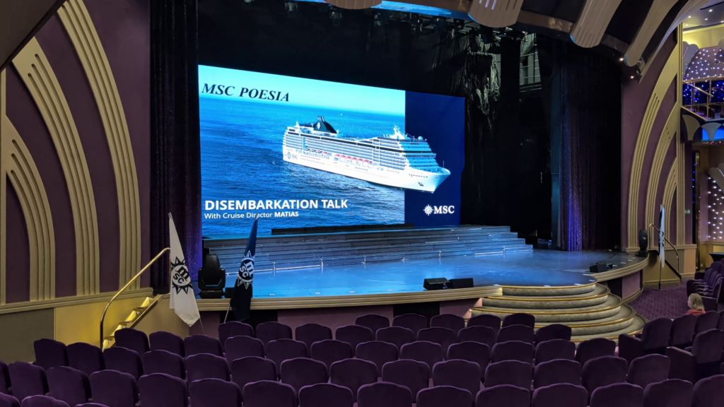 MSC Poesia theatre with a large screen displaying the disembarkation talk presentation with Cruise Director Matias during our Alaska cruise.