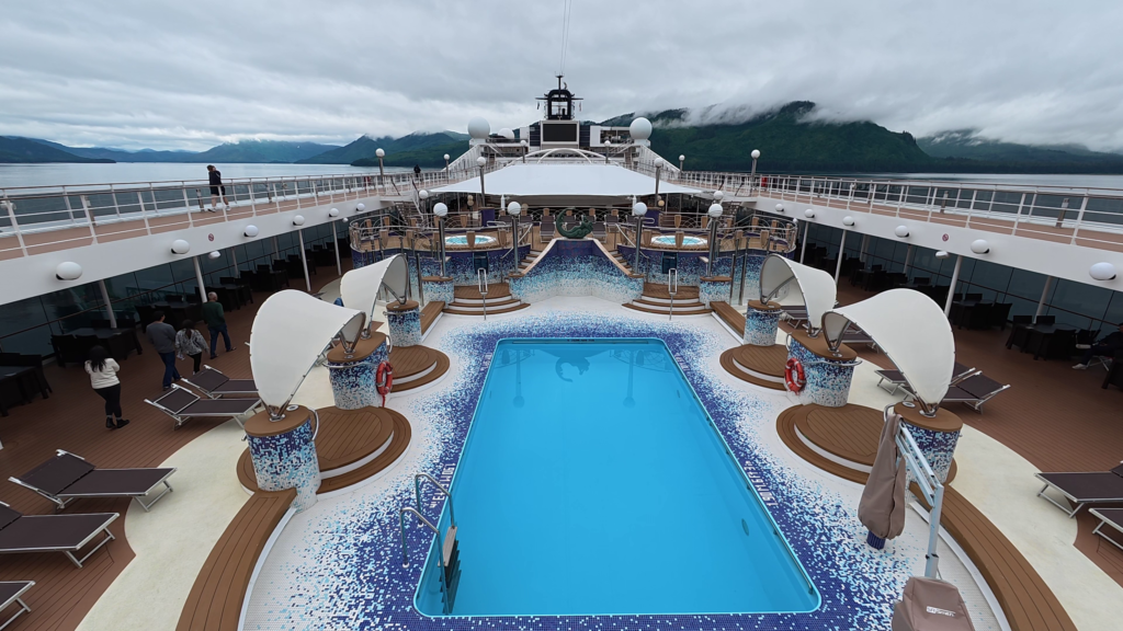 MSC Poesia outdoor swimming pool surrounded by loungers and raised hot tubs on Deck 13.