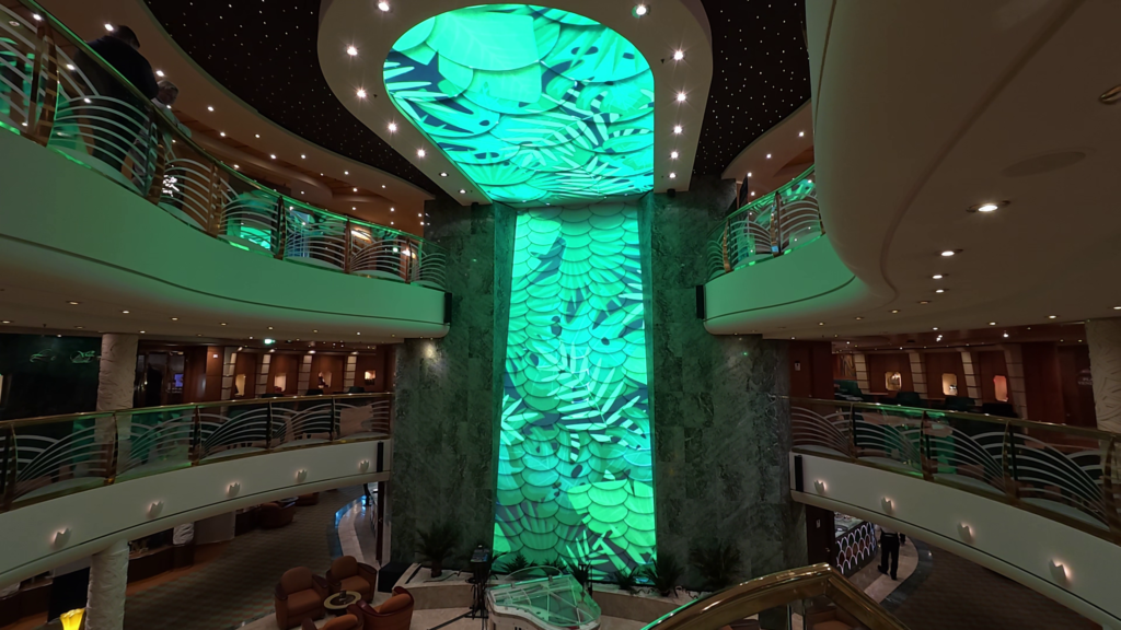 MSC Poesia three-story atrium with illuminated green wall and ceiling, curved balconies, and lounge seating.